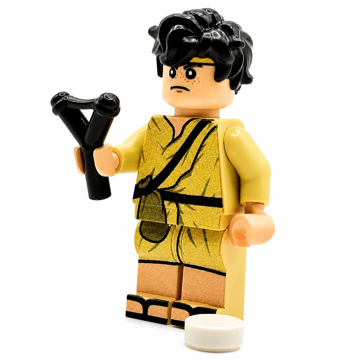 Custom Legos minifigure in gold gladiator outfit with black hair, holding a black slingshot.