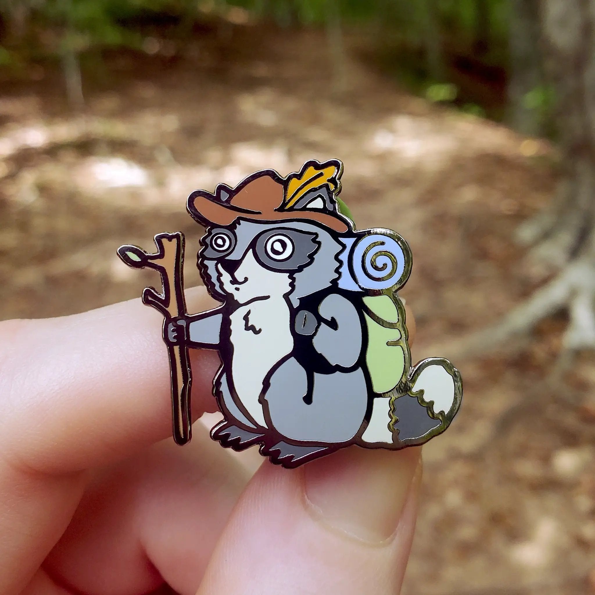 Kolorspun raccoon hiker pin featuring a detailed raccoon design on a small, collectible pin for hiking and outdoor enthusiasts.