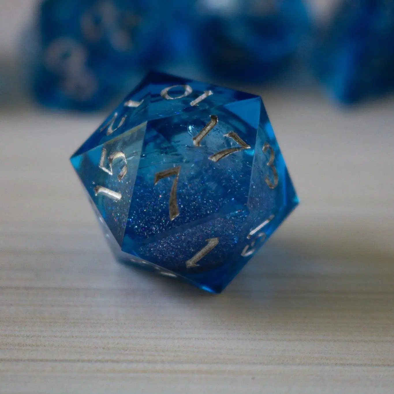 Blue glitter liquid core resin DND dice set with sharp edges, handmade by Runic Dice, featuring vibrant, sparkling blue hues.