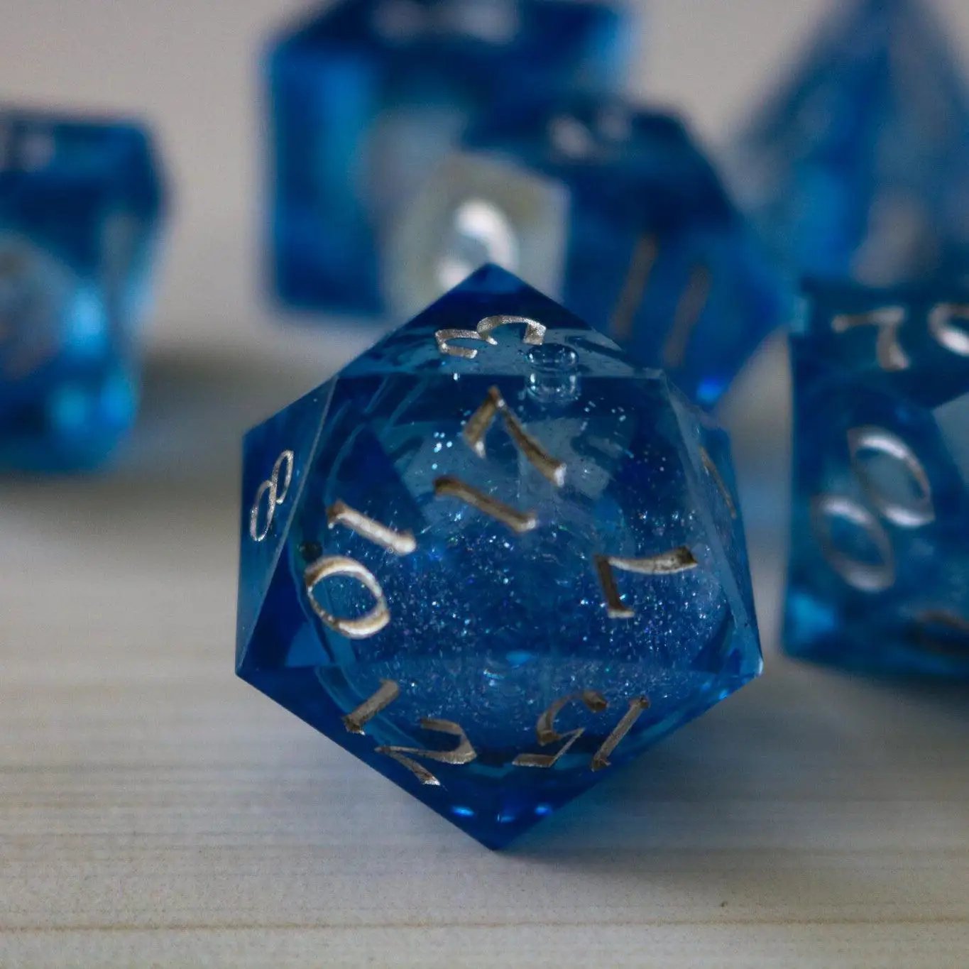 Blue glitter liquid core resin DND dice set with sharp edges, handmade by Runic Dice for tabletop gaming.
