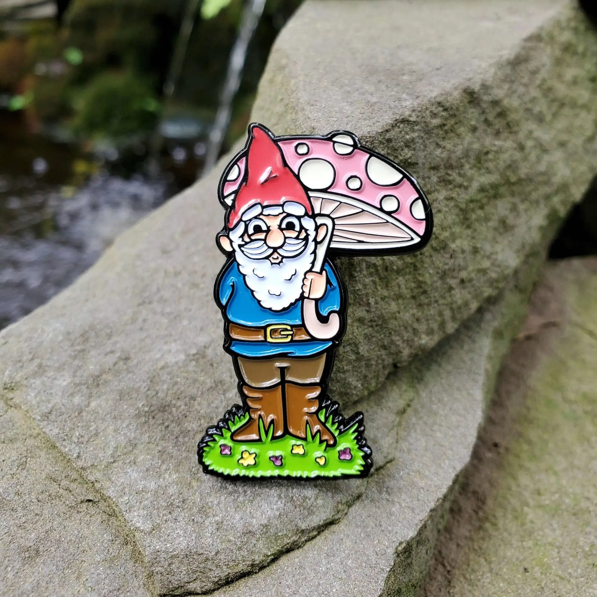 Kolorspun garden gnome enamel pin on rocks, featuring a whimsical garden gnome design for pin collectors and outdoor decor enthusiasts.