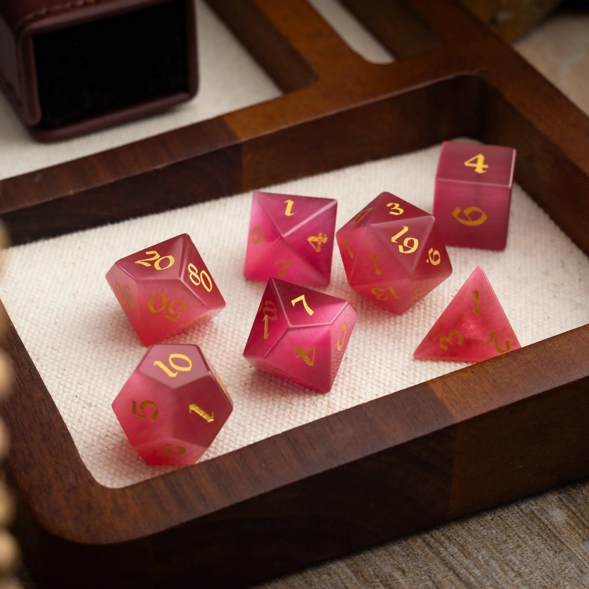 Hand-carved gemstone Rose Red Cats Eye DND dice set by Runic Dice, featuring vibrant, polished gemstone dice for tabletop gaming.