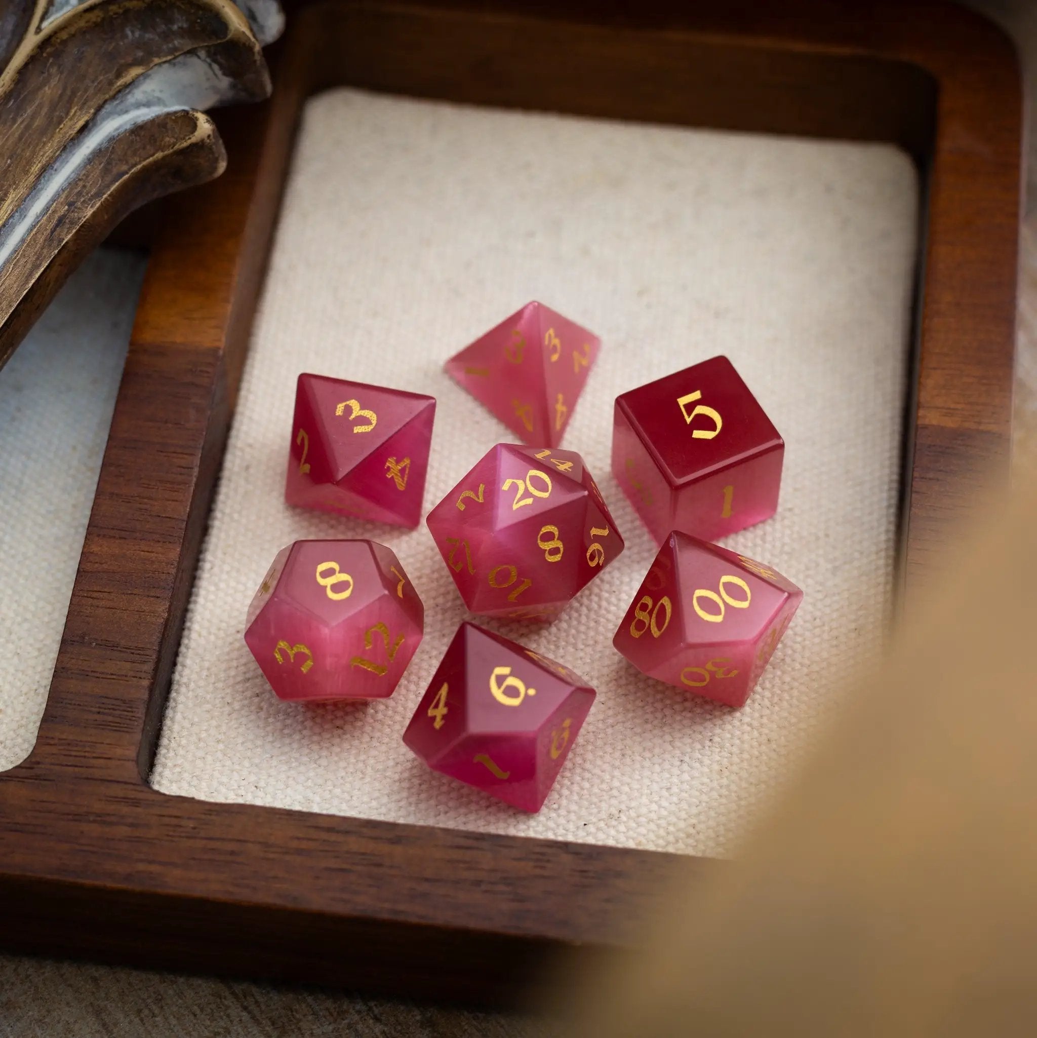 Hand-carved gemstone Rose Red Cats Eye DND dice set by Runic Dice, featuring six intricately designed gemstone dice for tabletop gaming.