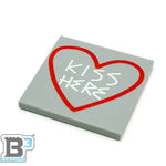 B3 Customs Kiss Here Road sidewalk art tile with white and red lettering on a concrete sidewalk surface.