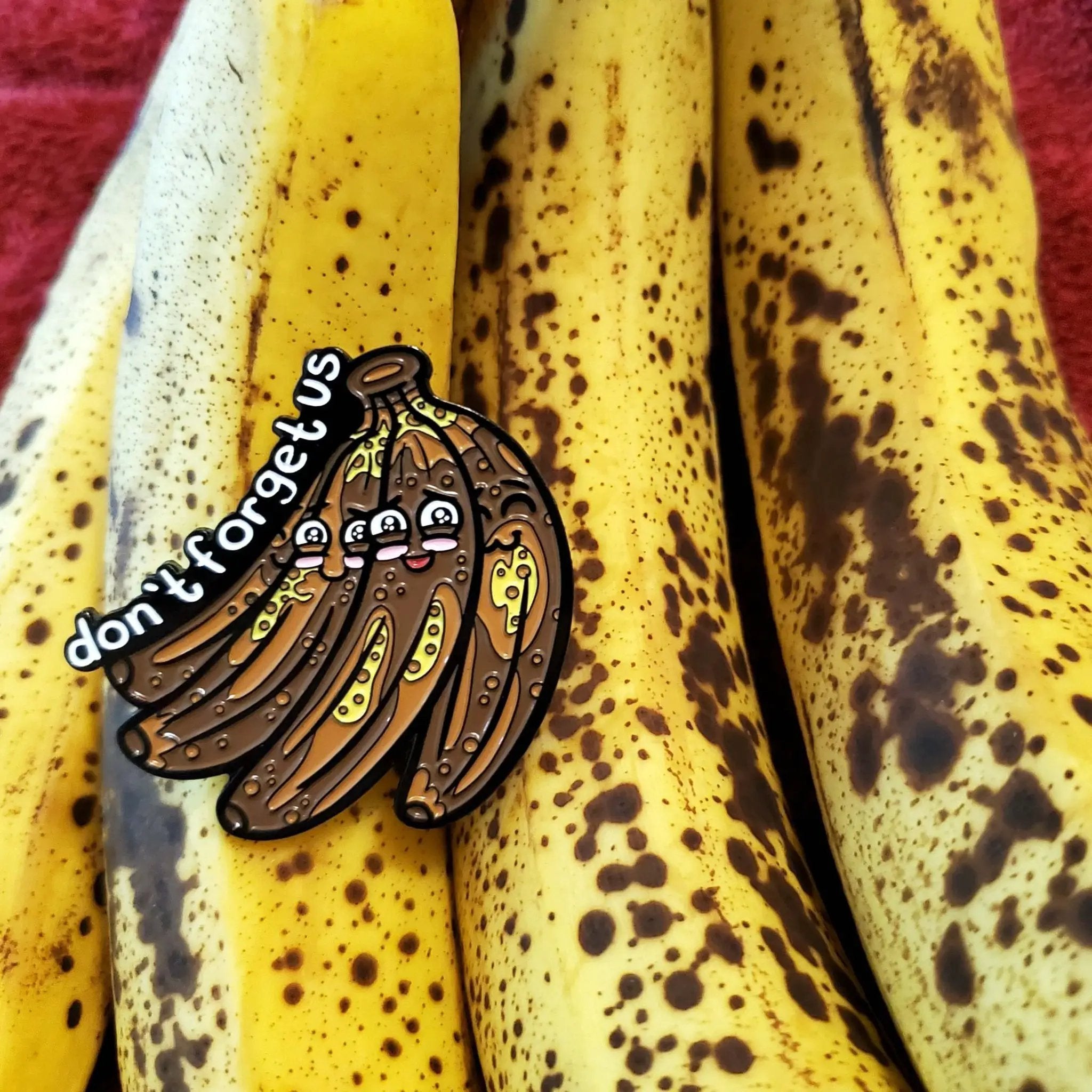 Kolorspun "Don't Forget Us" bananas enamel pin displayed on a white background, showcasing vibrant yellow banana design.