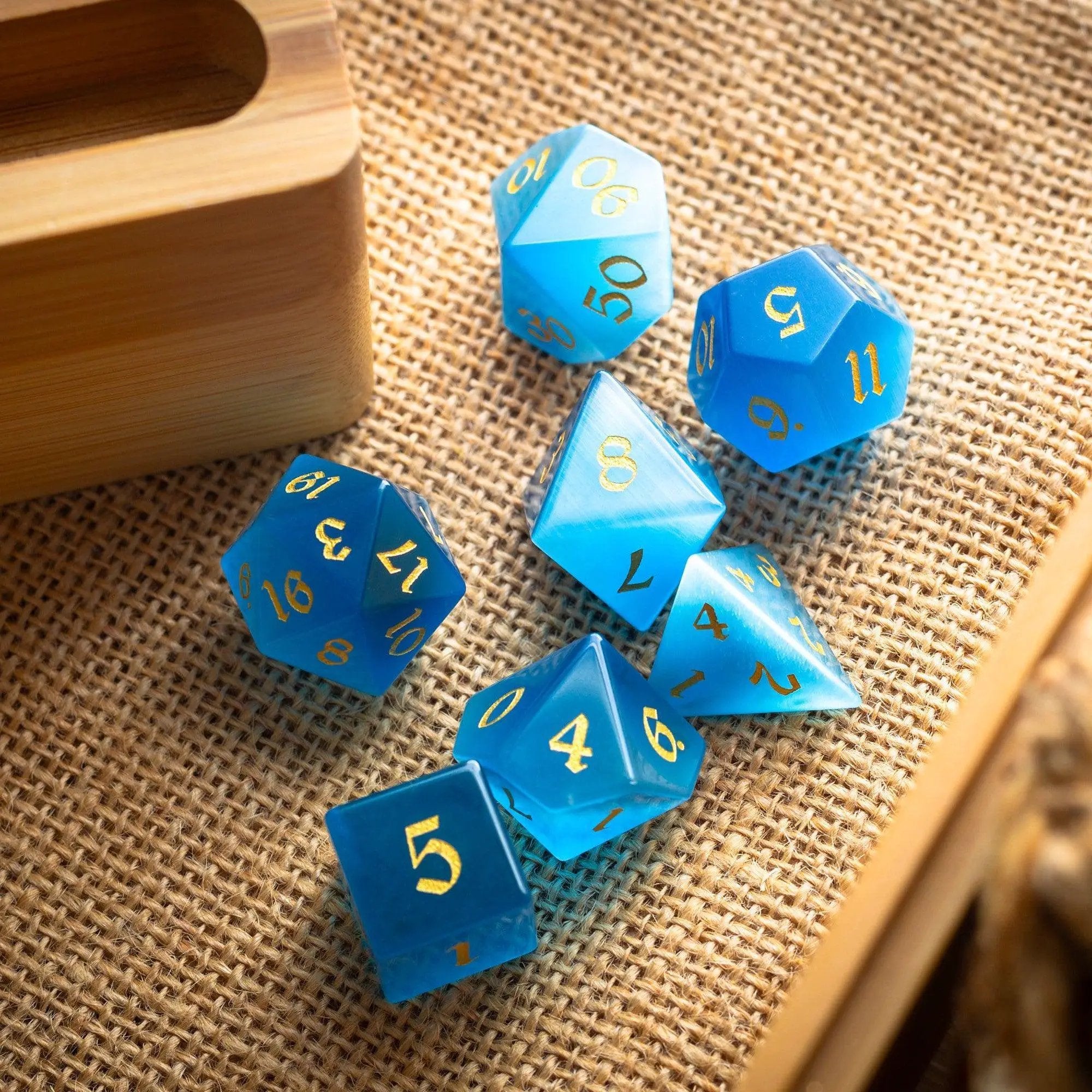 Light blue cats eye gemstone dice set hand-carved by Runic Dice, featuring intricate designs for tabletop gaming.
